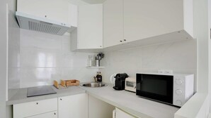 Una cucina moderna con mobili bianchi, un lavello in acciaio inossidabile, una macchina da caffè e un forno a microonde.