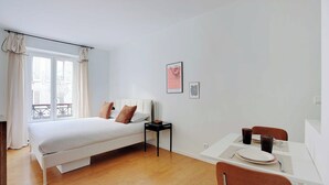 Una camera da letto con un letto, un comodino, un tavolino con un piatto e tazze, e una finestra con tende.