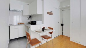 Una cucina compatta con mobili bianchi, un forno a microonde e un piccolo angolo ristoro con due sedie e un tavolo.