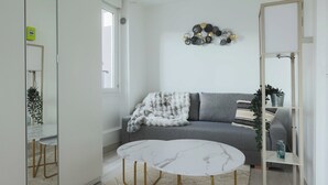 A modern living room with a grey sofa, a white round table, and a decorative wall piece. - Studio 2P Roland Garros/Parc des Princes (Boulogne-Billancourt)