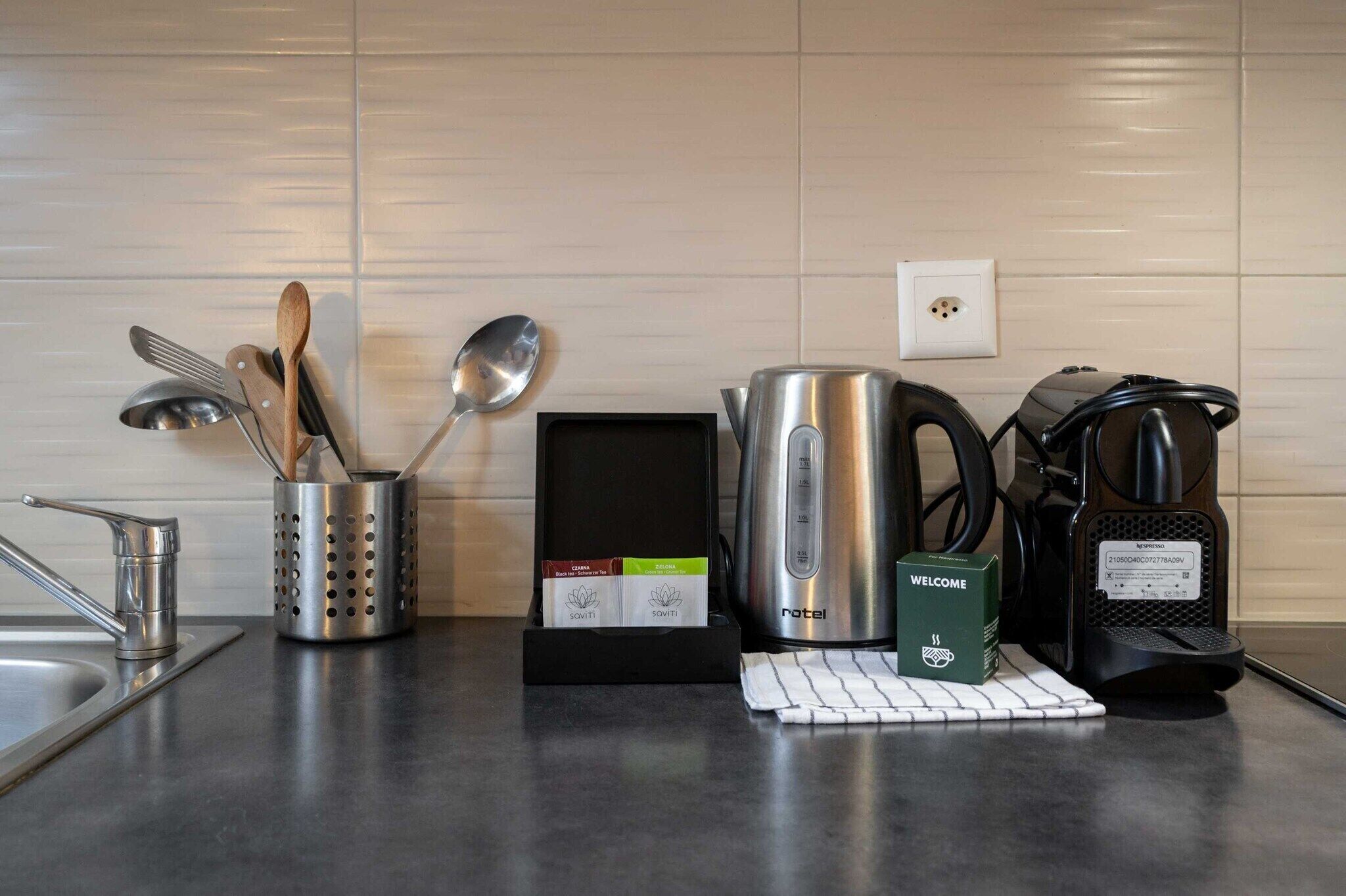 A kitchen counter with a coffee maker, a kettle, a box of tea bags, and a coffee machine.