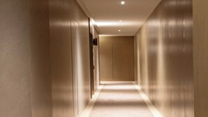 Un long couloir étroit, doté d’un plancher et de murs aux couleurs claires, qui mène à une porte au bout.