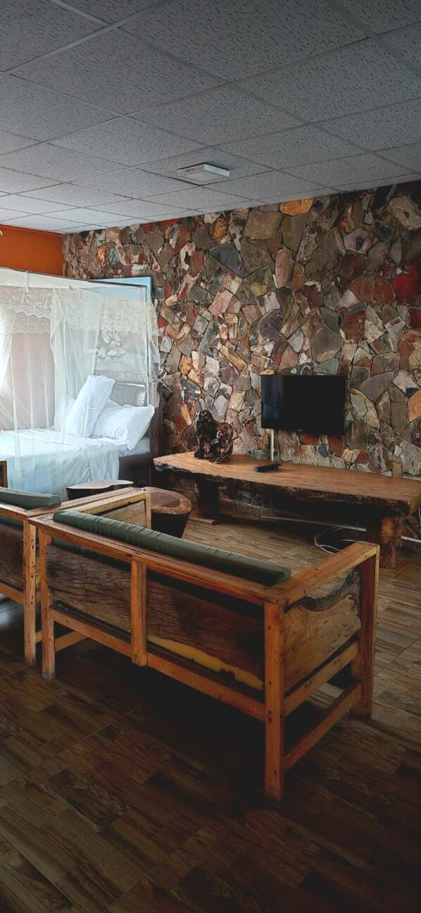 A room with a stone wall, a bed with a canopy, a wooden bench, and a television on a wooden stand.