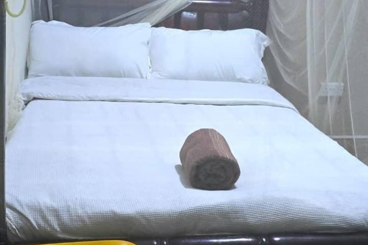 A single bed with white bedding, a mosquito net, and a yellow chair in a room with a tiled floor.
