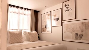Un dormitorio ordenado con una cama, una ventana con cortinas y tres obras de arte enmarcadas en la pared.