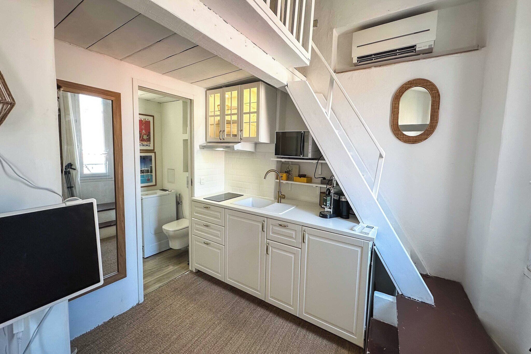 Una cocina con gabinetes blancos, microondas y pileta. Hay una escalera que lleva a otra habitación.