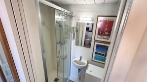 Un baño pequeño con cabina de ducha de vidrio, un lavamanos y un espejo.