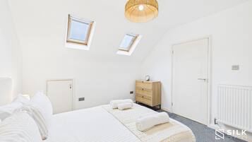 A bedroom with a large bed, a dresser, a skylight, and a ceiling light.