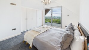 A bedroom with a large bed, a chandelier, a view through a sliding door, and a wardrobe.
