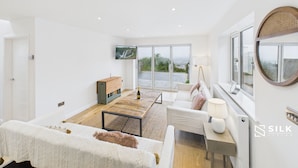 A spacious living room with a large window, a flat-screen TV, a wooden coffee table, and a sofa with a throw blanket.