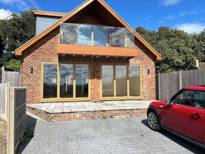 Une maison à deux étages avec une façade en briques, de grandes fenêtres et une voiture rouge garée dans l’allée.