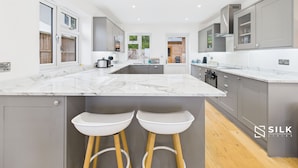 A modern kitchen with marble countertops, grey cabinetry, and a central island with stools.