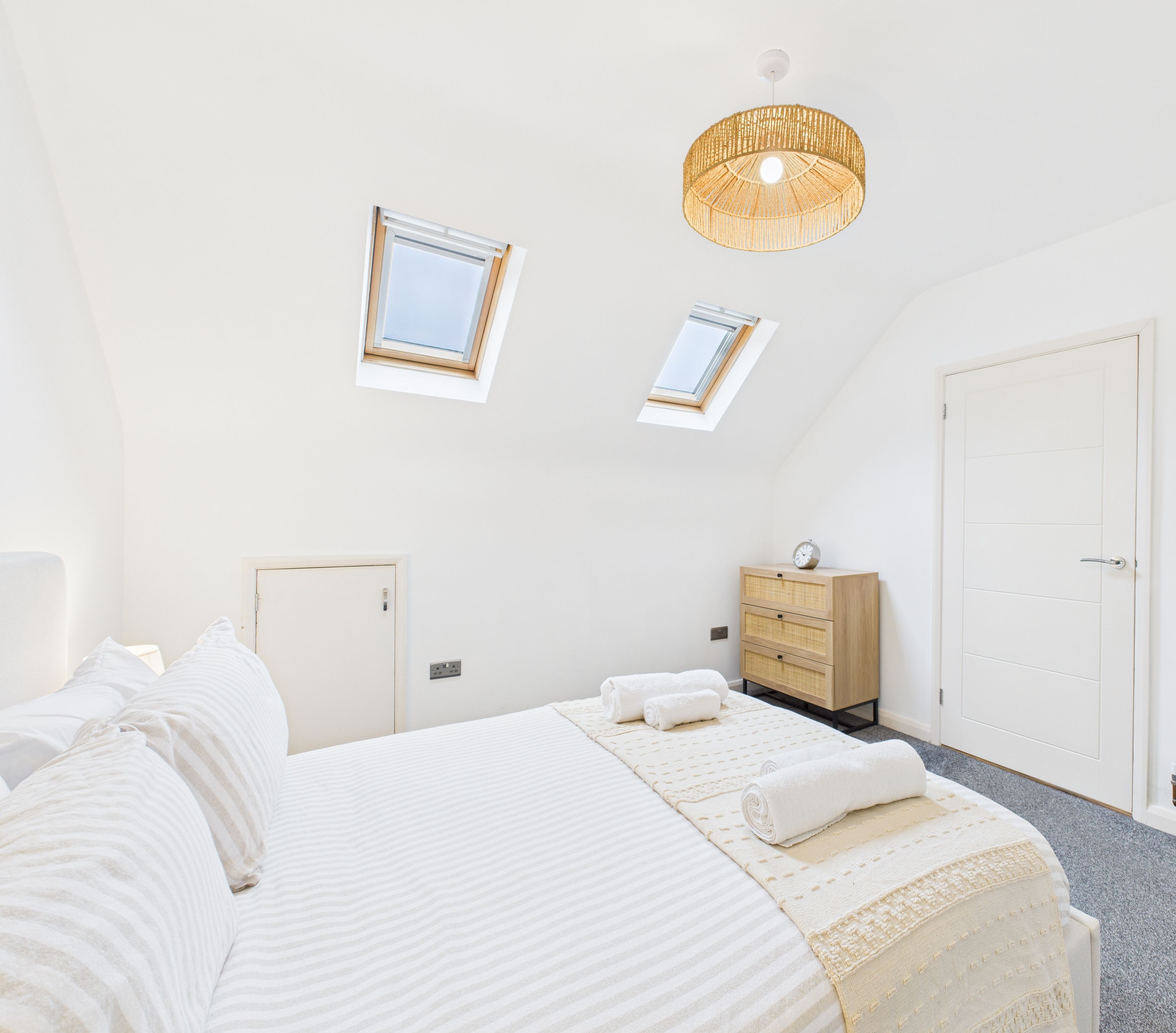 A bedroom with a large bed, a dresser, a skylight, and a ceiling light.