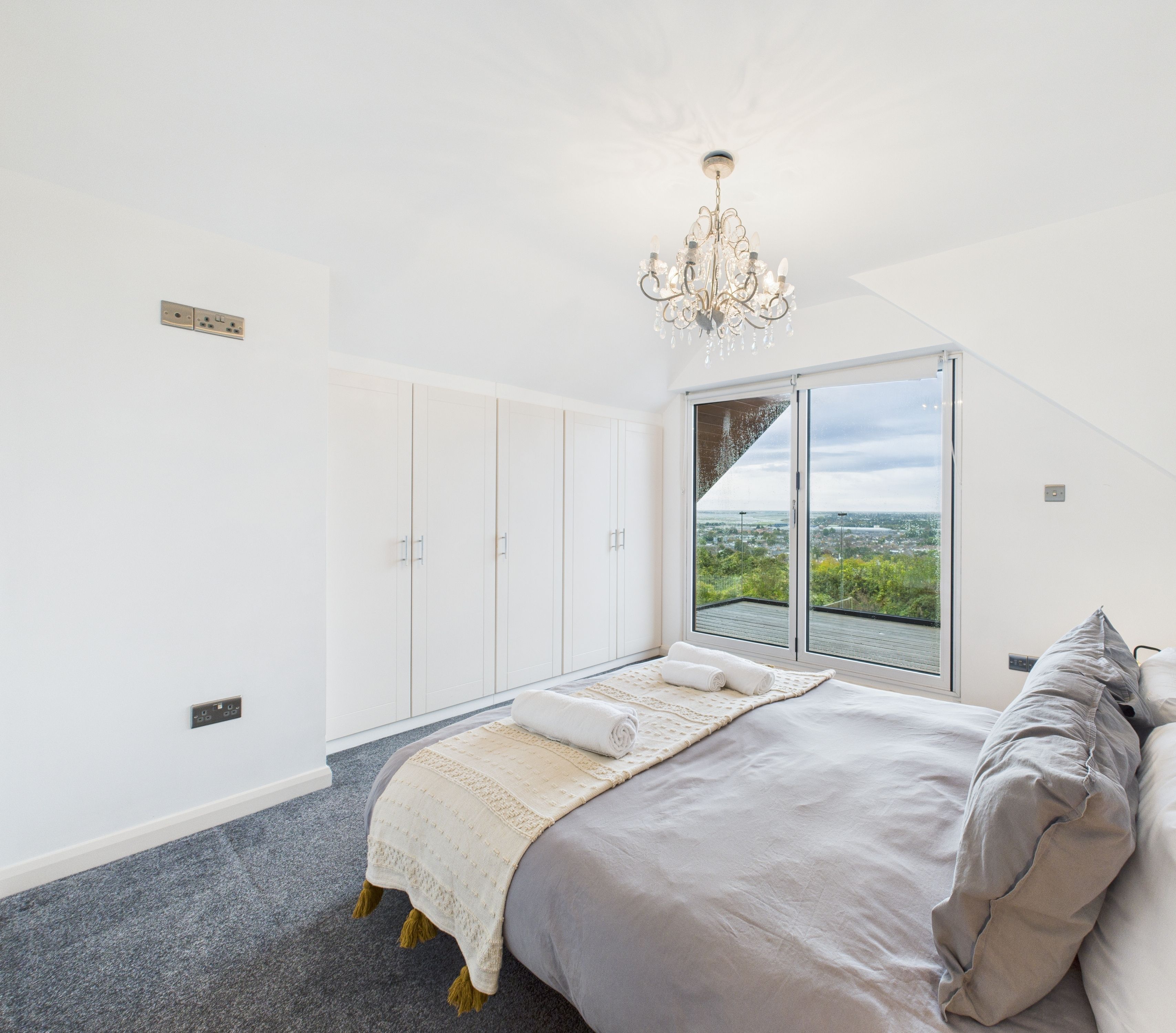 A bedroom with a large bed, a chandelier, a view through a sliding door, and a wardrobe.