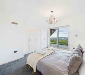Un dormitorio con una cama grande, un candelabro, vistas a través de un ventanal corredero y un armario.