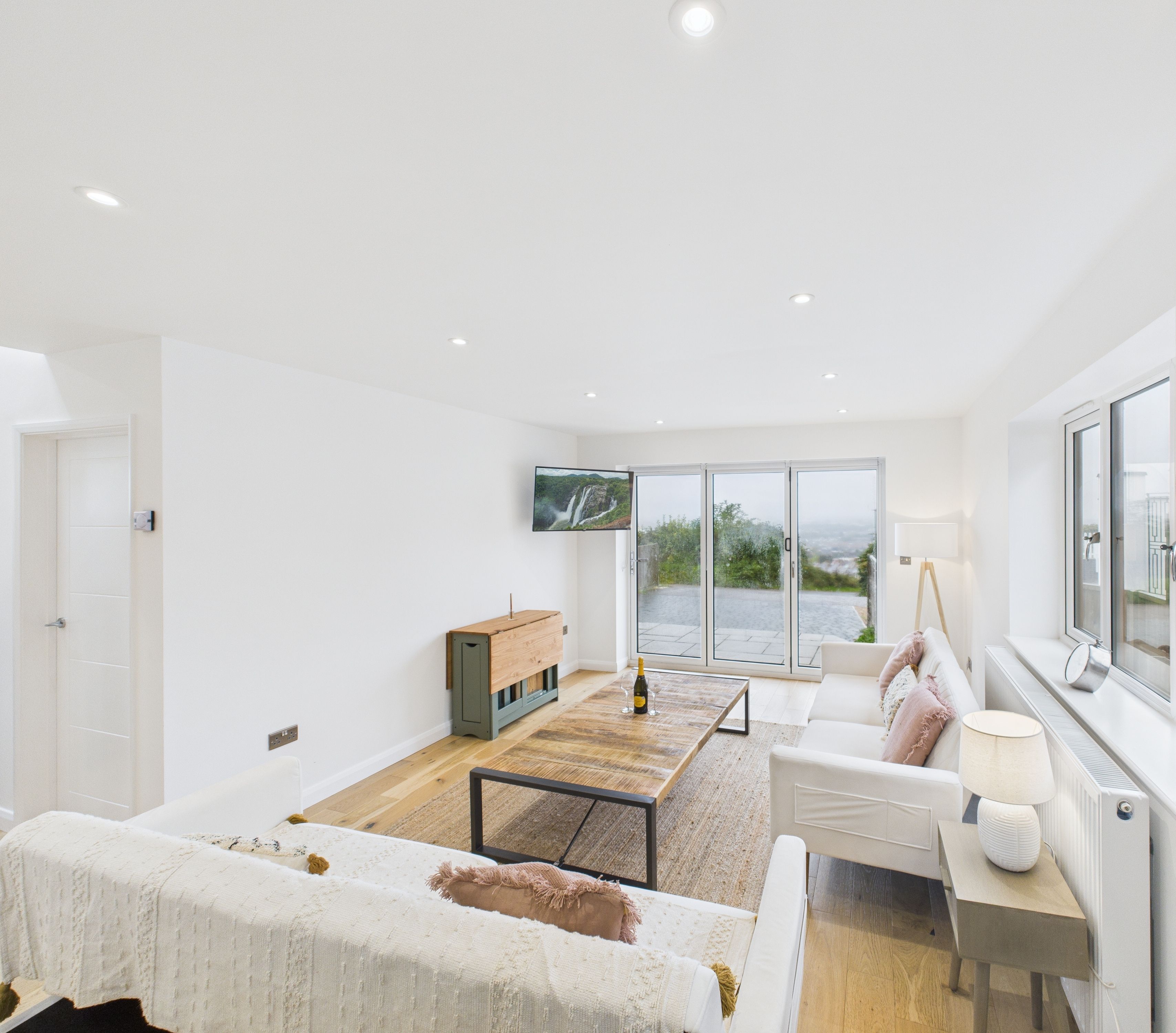 A spacious living room with a large window, a flat-screen TV, a wooden coffee table, and a sofa with a throw blanket.