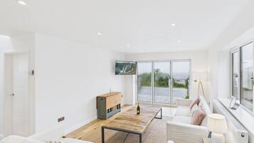 A spacious living room with a large window, a flat-screen TV, a wooden coffee table, and a sofa with a throw blanket.