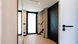 A hallway with a wooden floor, a dark door, and a staircase leading to another room.