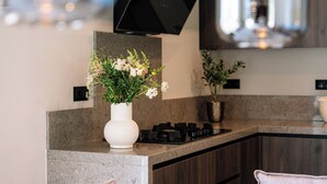 A modern kitchen with a flat-screen TV mounted above the counter, a white vase with flowers, and a gas stove.