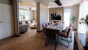 A modern living room with a large dining table, leather chairs, a sofa, and a television.