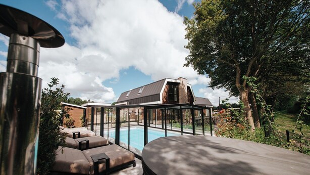 Een modern buitenzwembad met loungebedden en een jacuzzi, omgeven door bomen en een groot huis op de achtergrond.