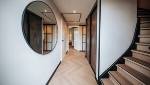 Een moderne hal met een houten trap, een ronde spiegel en een visgraatparket.