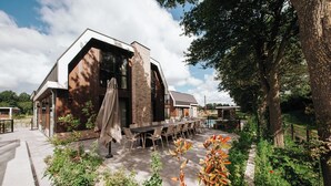 Een modern gebouw met een ruim terras, buitenmeubilair en een tuin.