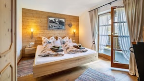Une chambre à coucher avec une tête de lit en bois, un lit agrémenté de plusieurs oreillers, des lampes de chevet, une fenêtre avec des rideaux et une vue sur l’extérieur.