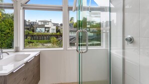 A modern bathroom with a glass shower door, a sink, and a view of neighboring houses.