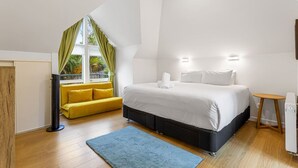 A bedroom with a bed, a yellow sofa, a blue rug, and a window with curtains.