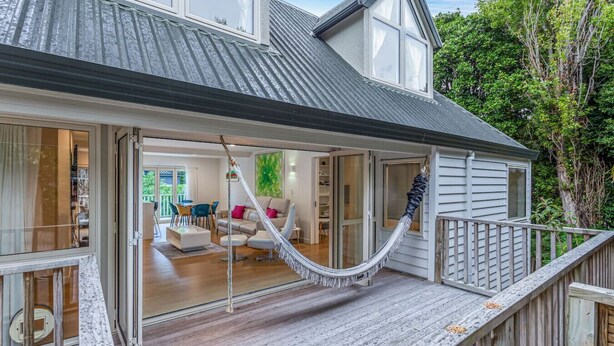 A modern house with a large porch, a hammock, and a dining area visible through the open door.