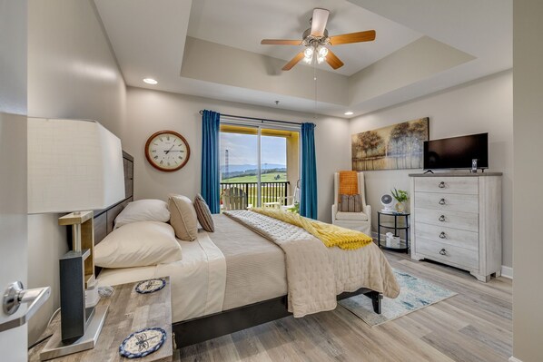 A bedroom with a bed, a ceiling fan, a TV, a dresser, and a window with curtains.