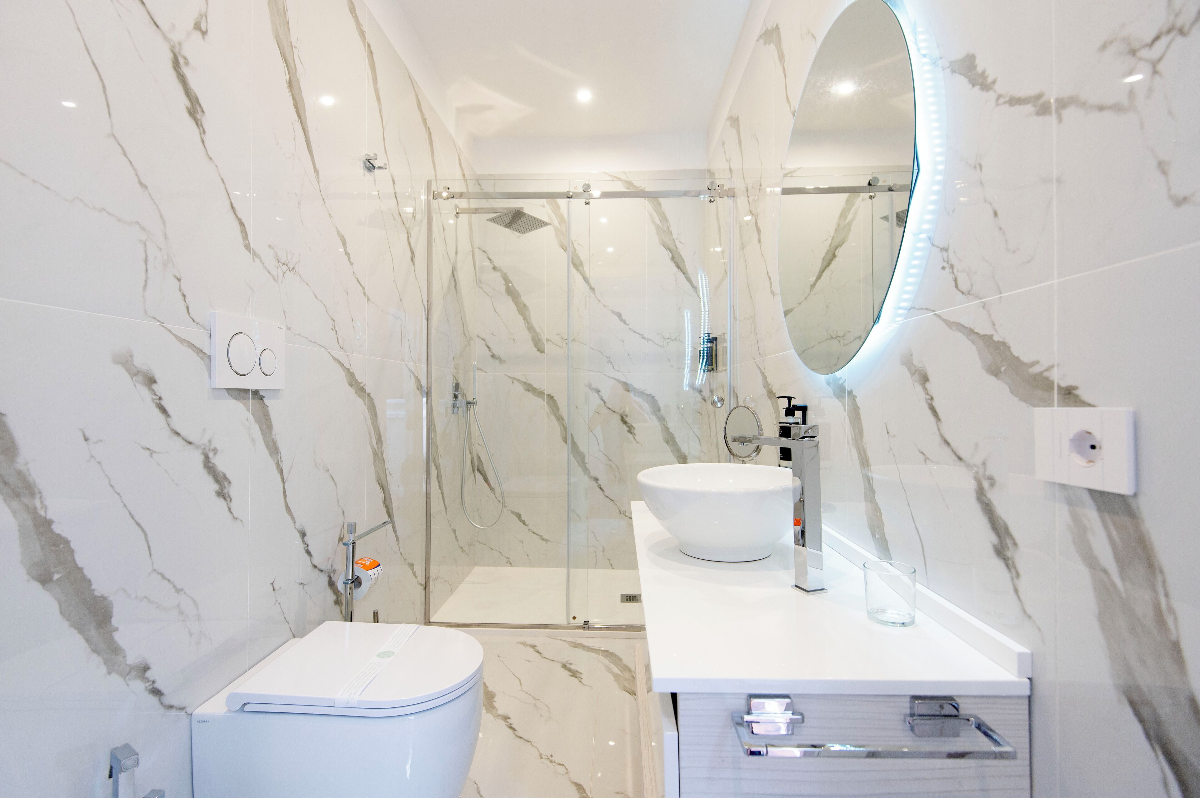 Ein modernes Badezimmer mit einer gläsernen Dusche, einem weißen Waschbecken und einem großen Spiegel.