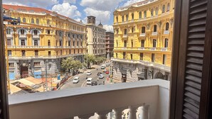 A view from a balcony overlooking a street with historic yellow buildings, a clear sky, and a few pedestrians. - Naples Plaza Duomo (Naples)