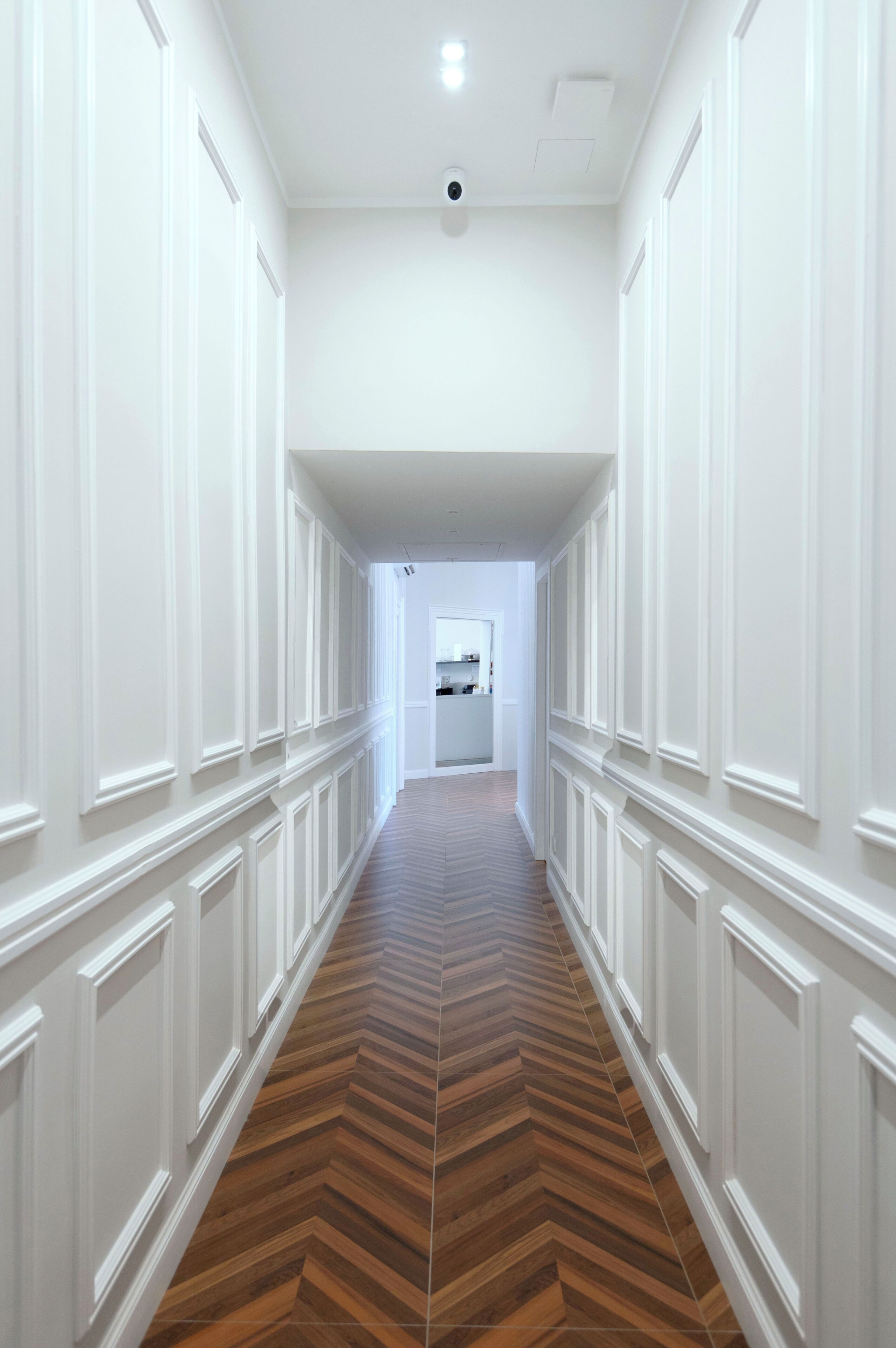 Um corredor com lambris brancos e piso de madeira em padrão herringbone.