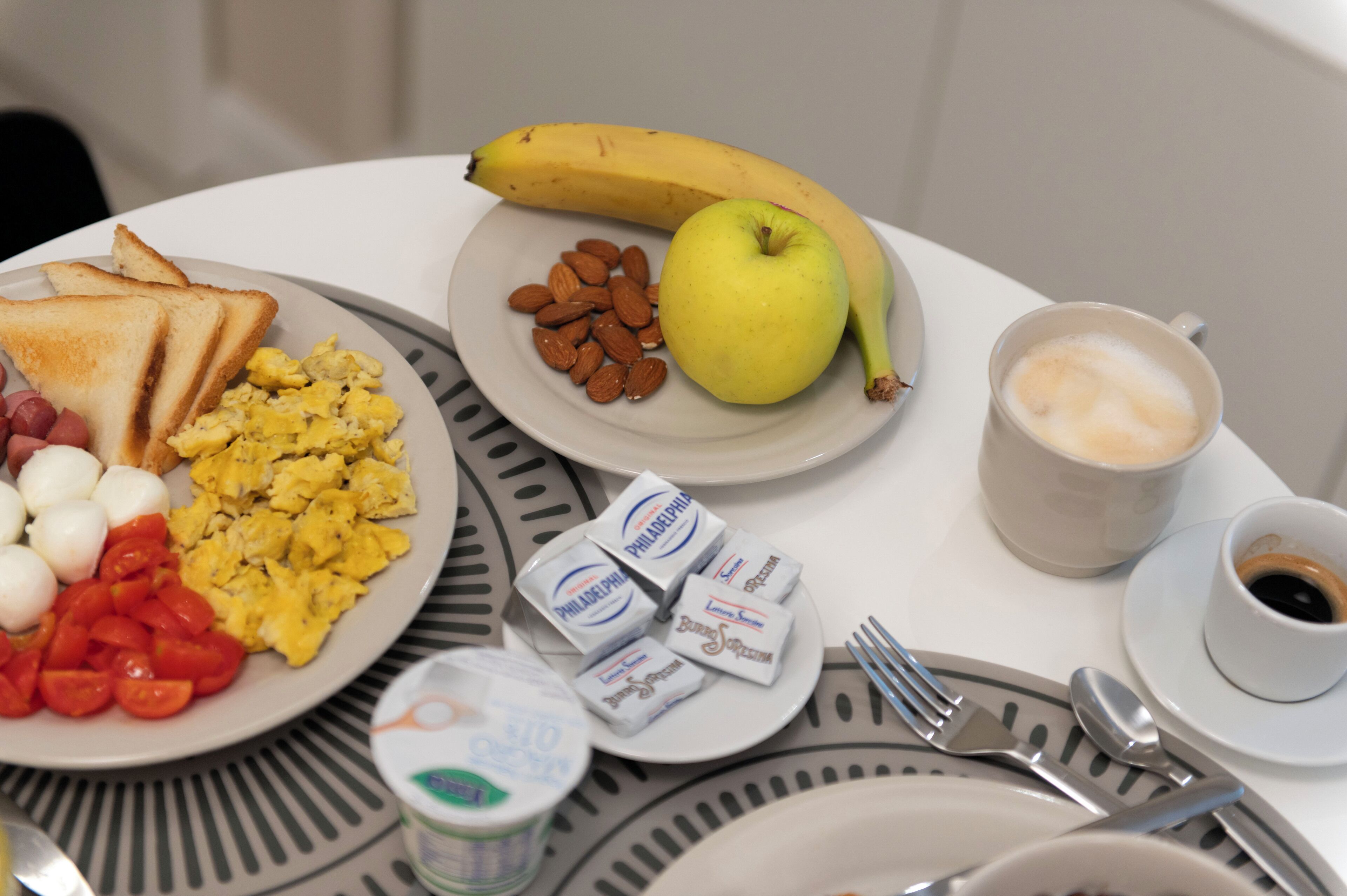 Une assiette de petit-déjeuner comprenant des toasts, des œufs, des tomates, des amandes, une banane et une pomme.