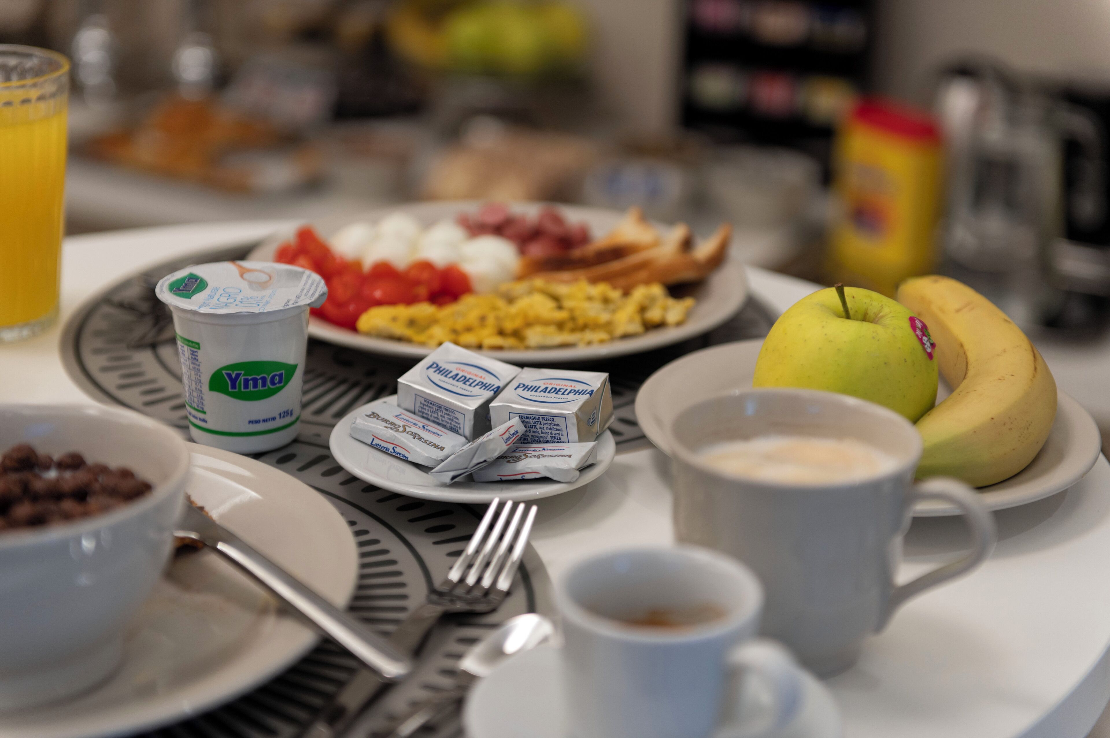 A breakfast table with plates of food, a glass of orange juice, a banana, and a cup of coffee.