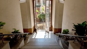 A grand staircase leading to an outdoor balcony with a view of a garden and buildings. - Naples Plaza Duomo (Naples)