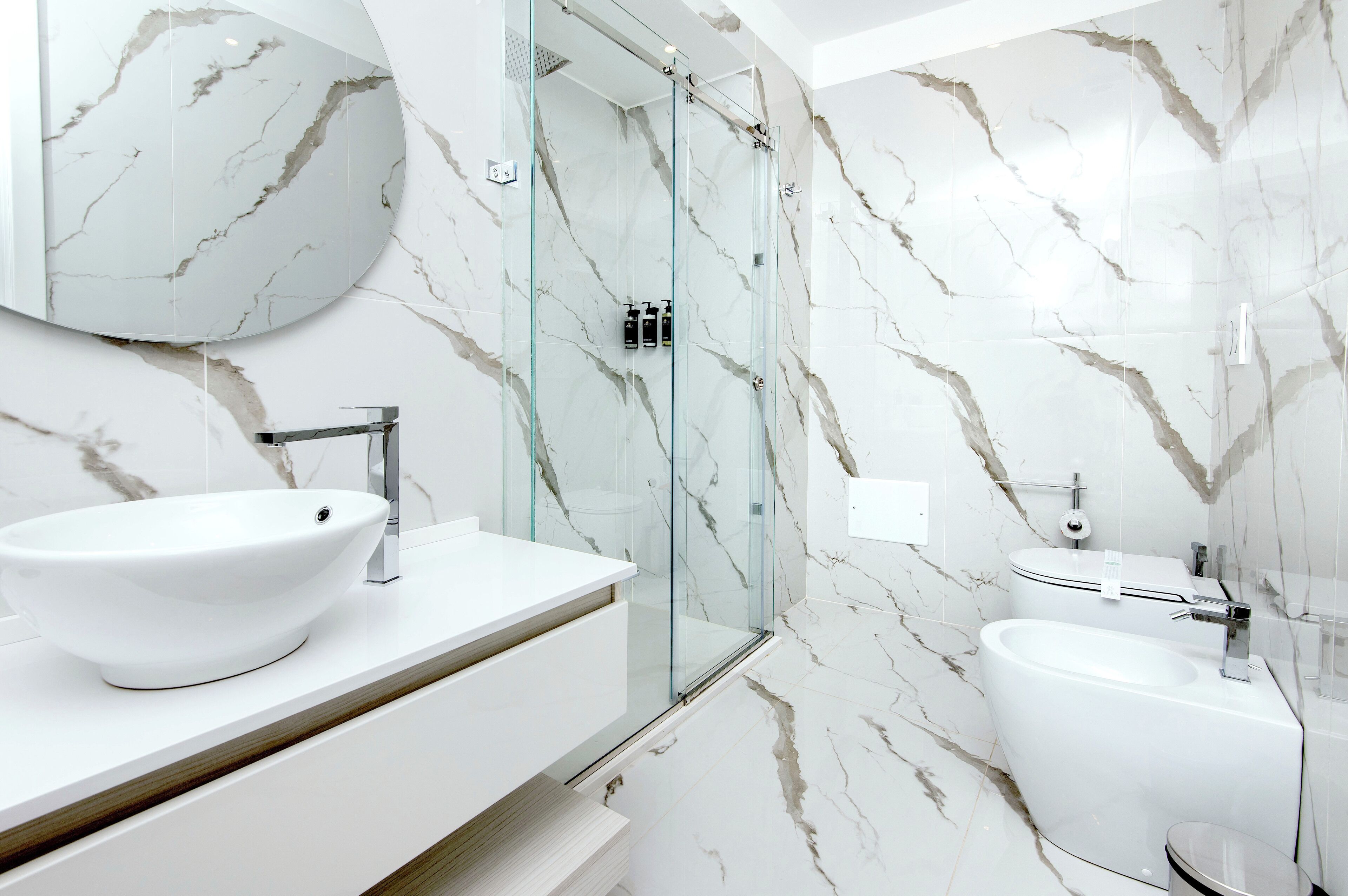 A modern bathroom with a large white sink, a glass-enclosed shower, and a toilet.