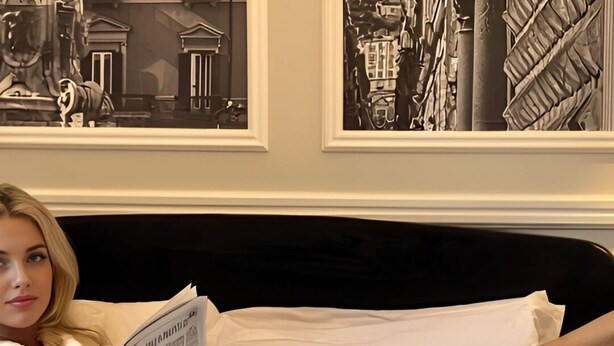 A person reading a newspaper in a white bathrobe on a bed with a tray of pastries, a glass of milk, and a red rose. - Naples Plaza Duomo (Naples)