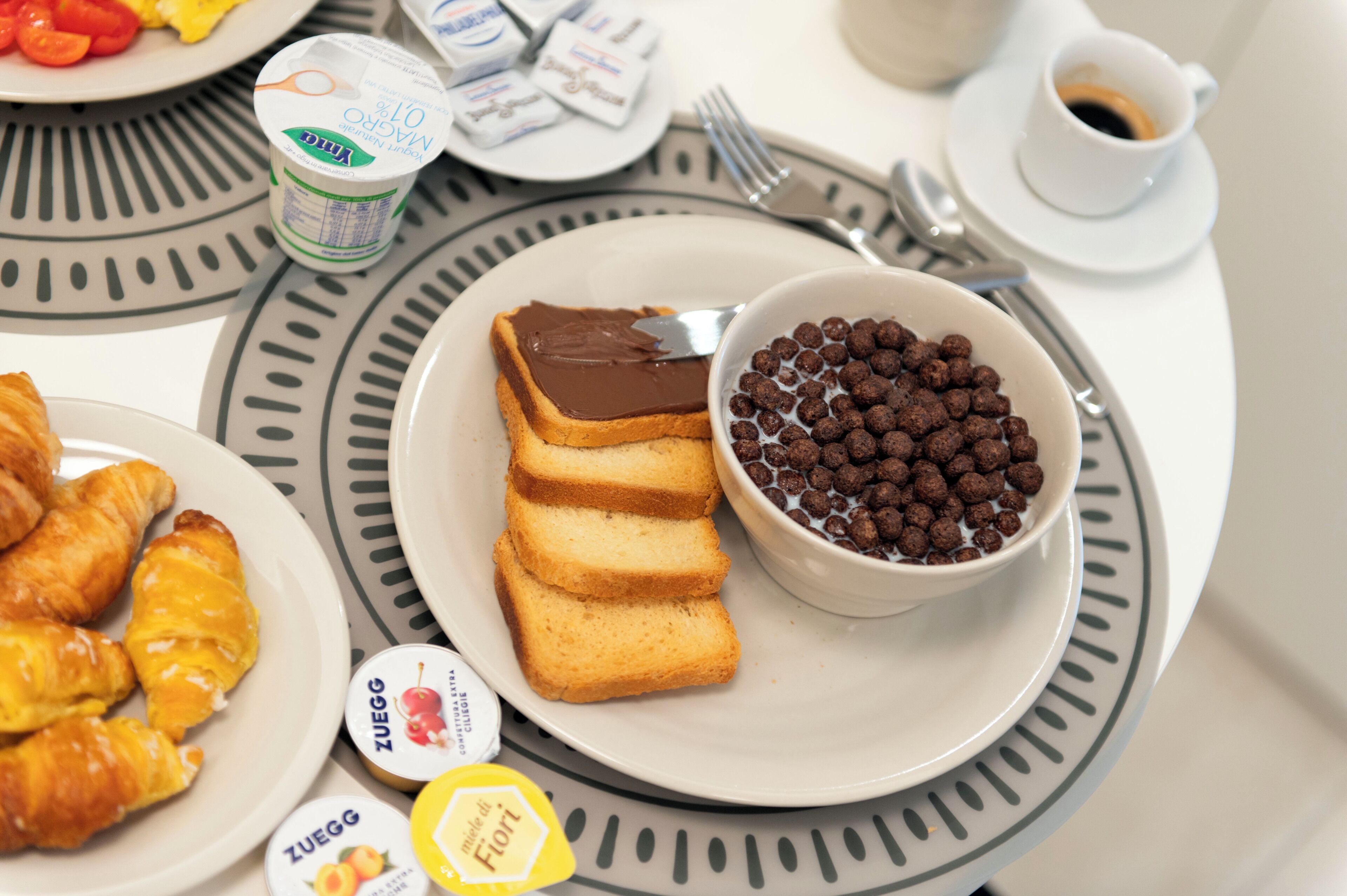 Een ontbijttafel met croissants, chocoladepasta en chocoladebolletjes op borden.