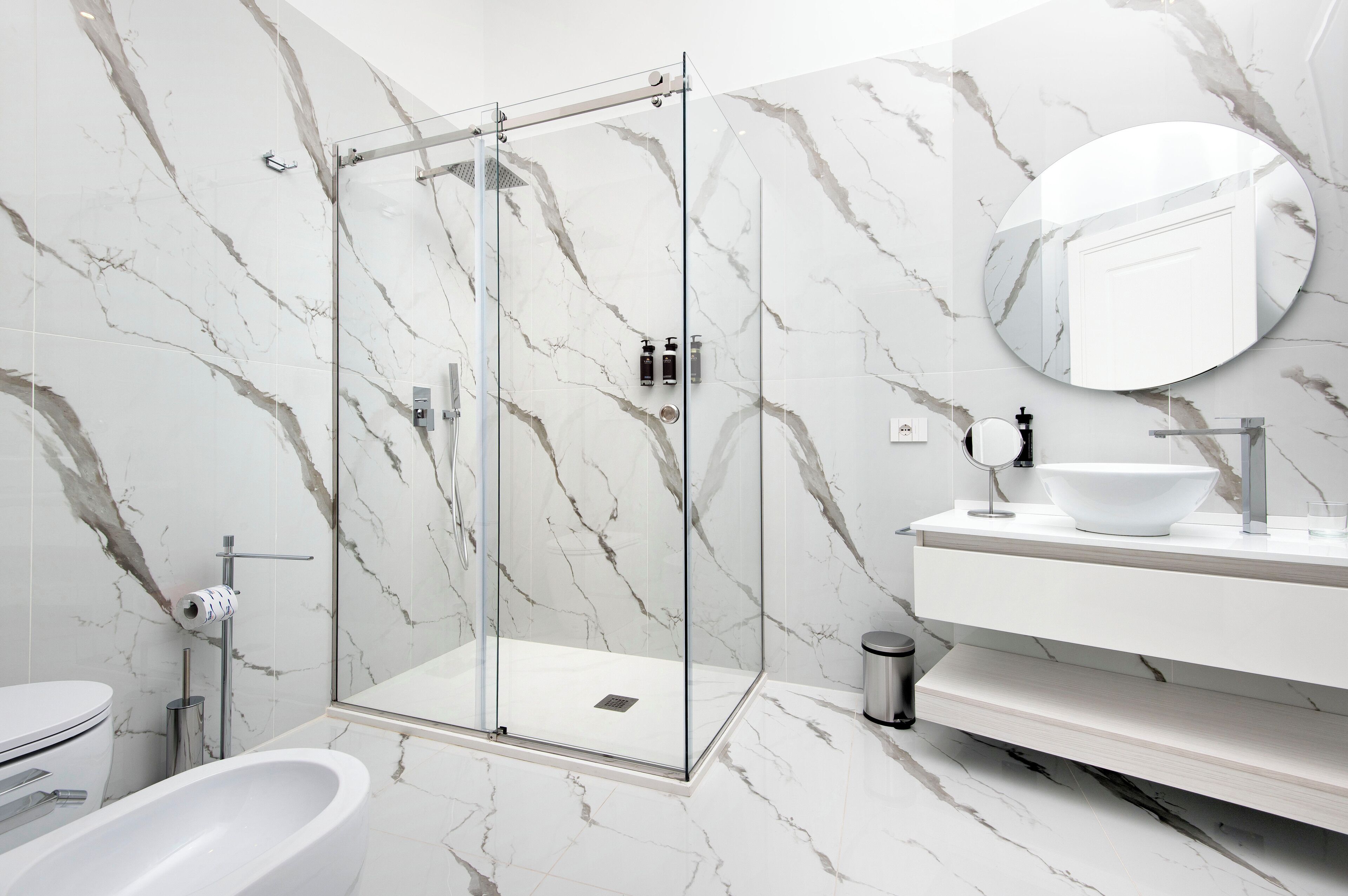 Ein modernes Badezimmer mit einer gläsernen Duschkabine, einem weißen Waschbecken und einer Wand mit Marmorfliesen.