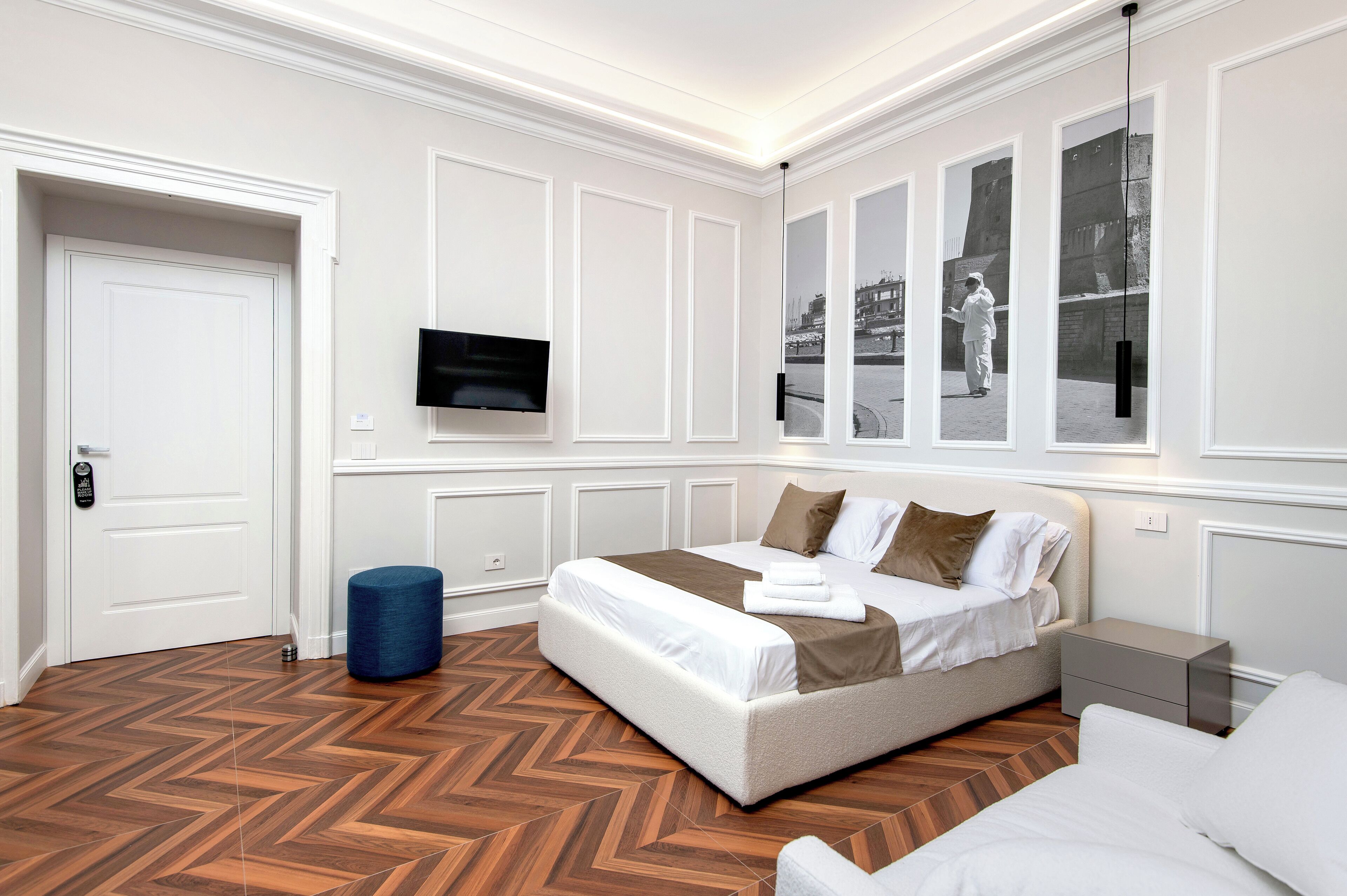 A modern hotel room with a large bed, a flat-screen TV, and a view of a cityscape through the windows.