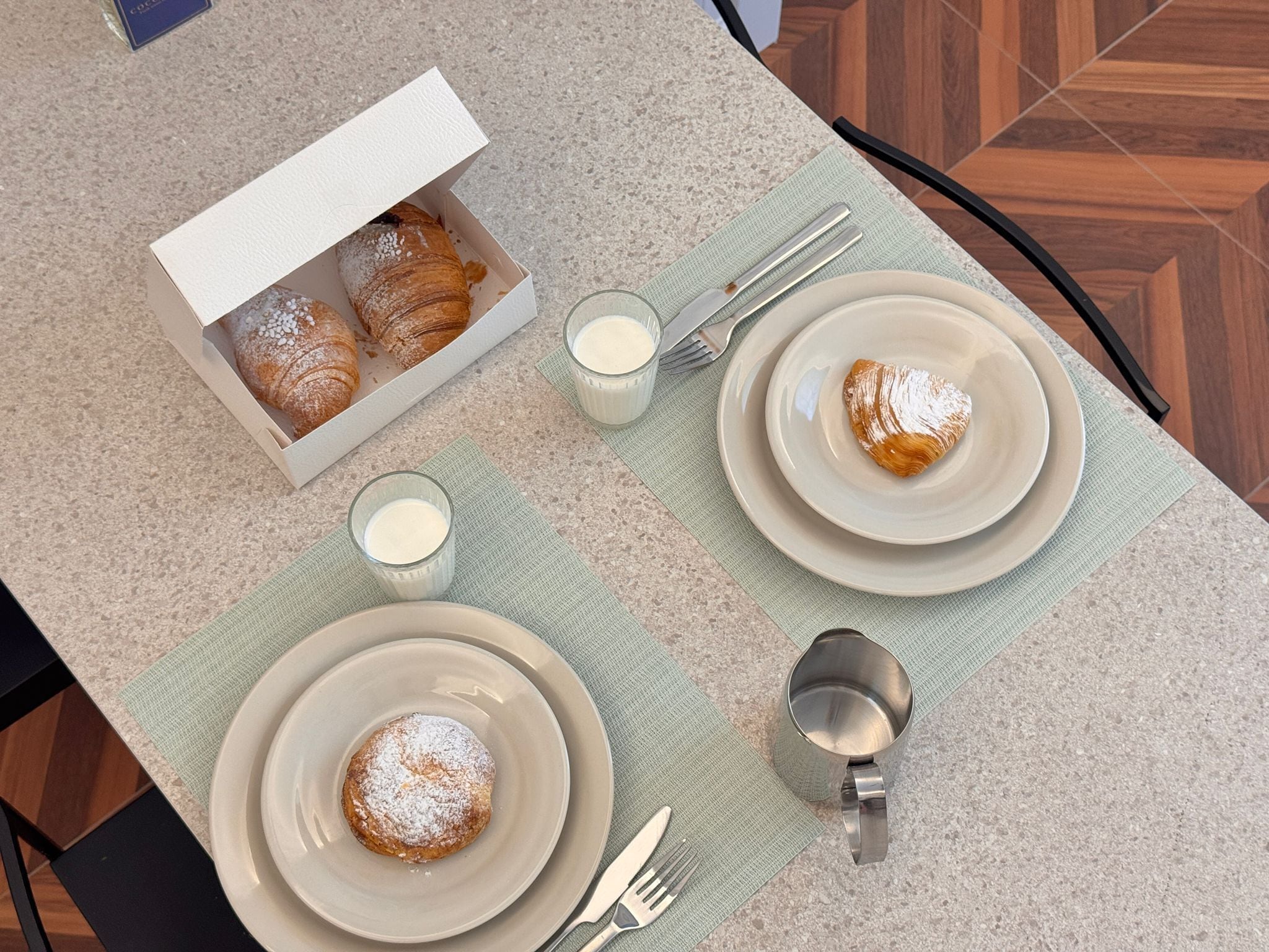 A breakfast setting with croissants, milk, and a coffee cup on a table.