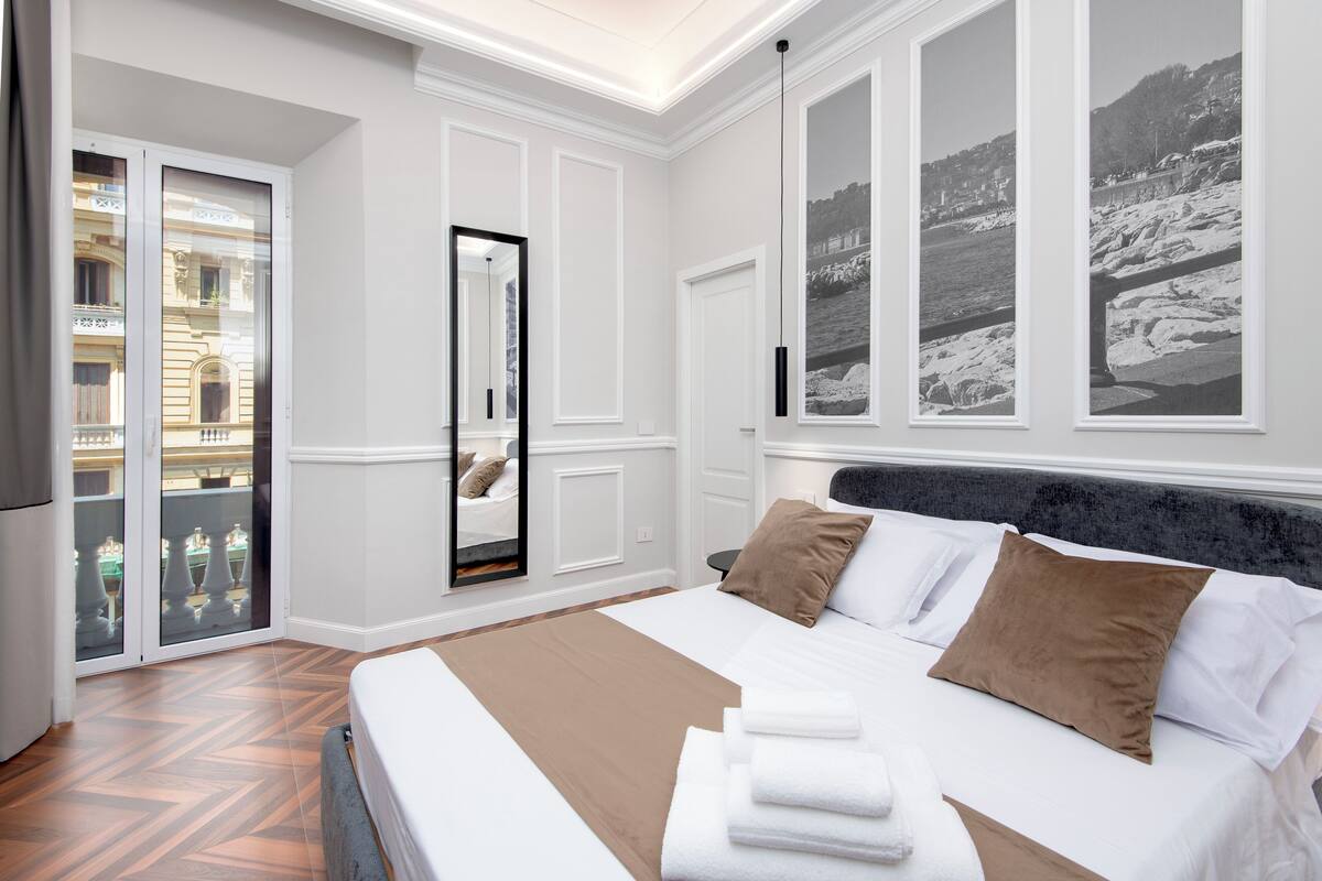 A hotel room with a large bed, a view of the city through a balcony, and a black and white photo on the wall.