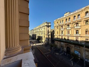 A view from a window overlooking a street with classical architecture, including a building with arched windows and a balcony. - Naples Plaza Duomo (Naples)