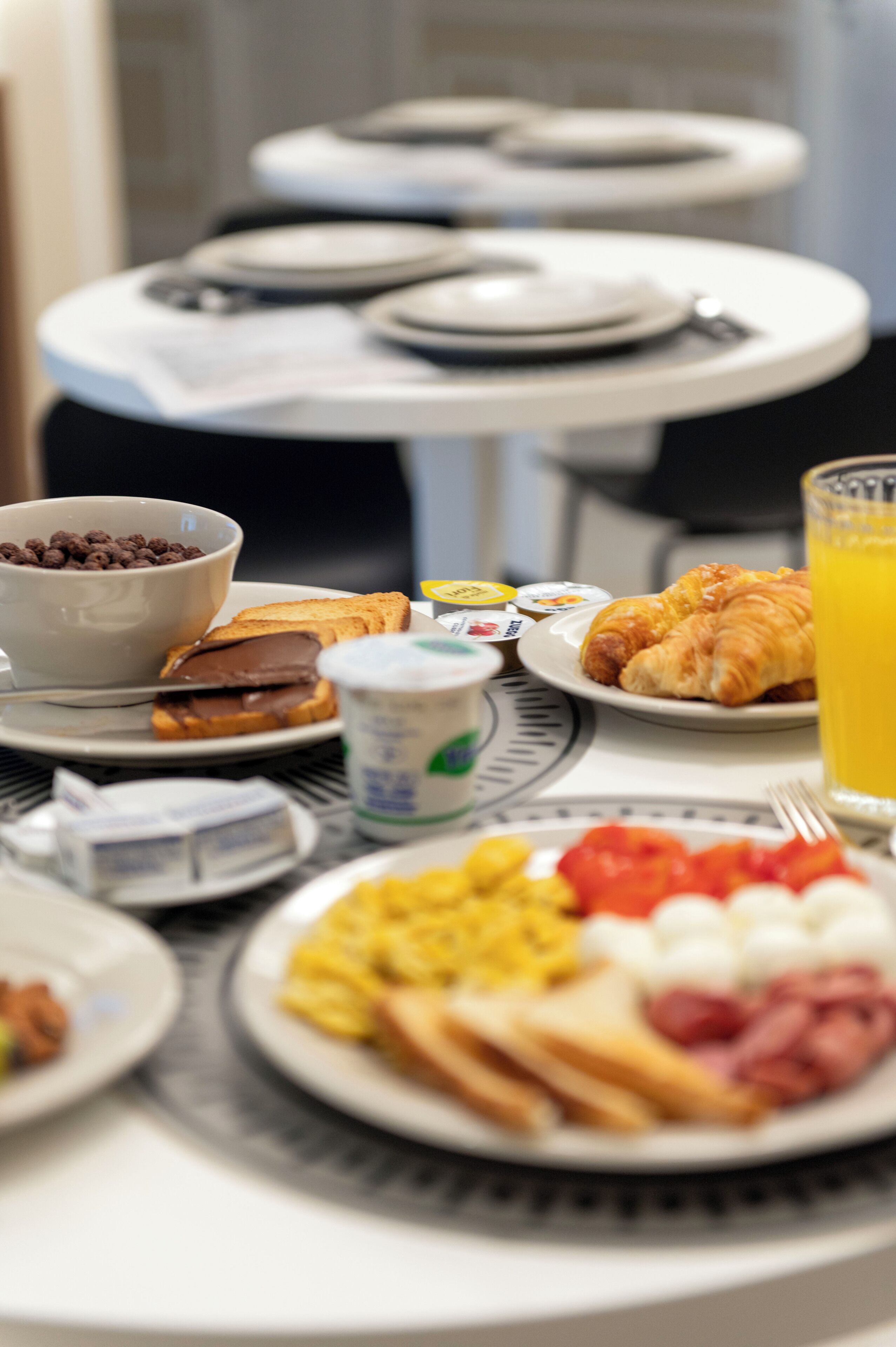 A breakfast table with plates of food, a bowl of cereal, and a glass of orange juice.