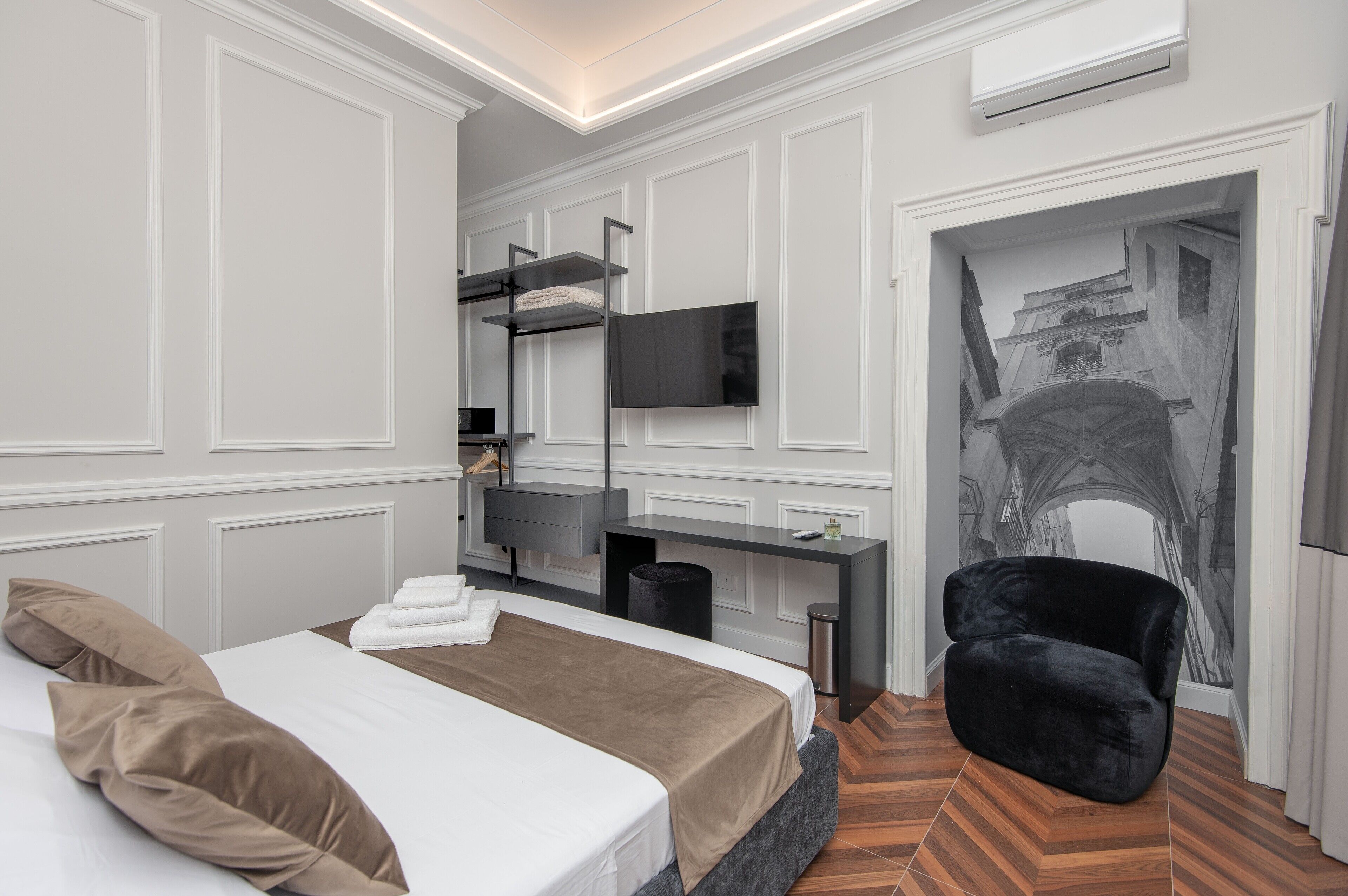 Une chambre d’hôtel moderne équipée d’un lit, d’un téléviseur à écran plat fixé au mur, d’une chaise noire et d’une fresque murale originale.