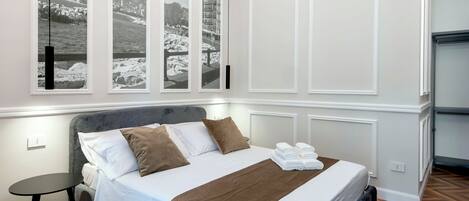 A neatly arranged bedroom with a bed, pillows, a bedside table, and a view of a snowy landscape through large windows.