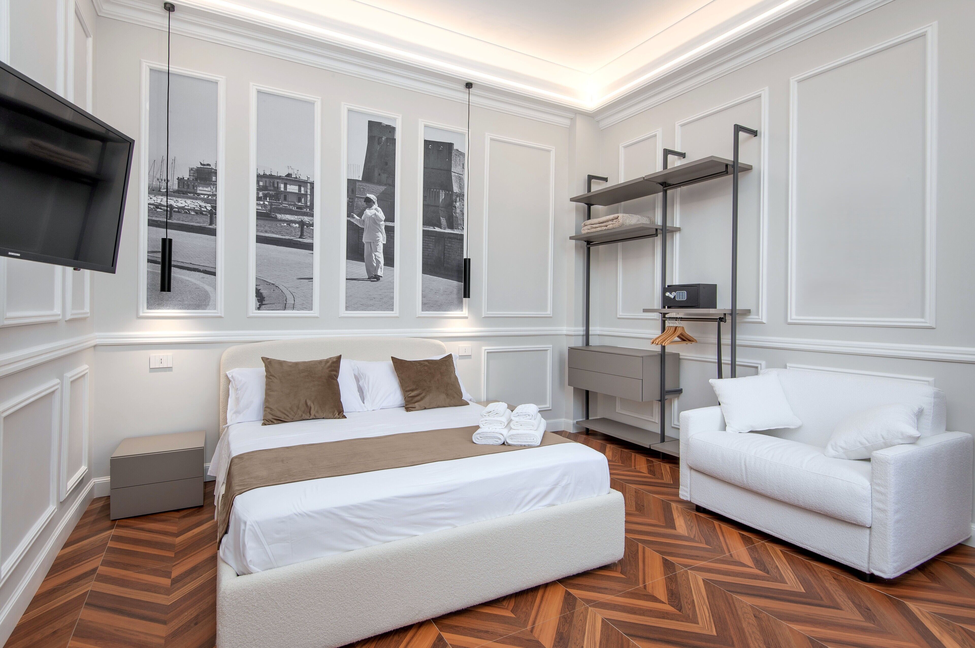 A hotel room with a bed, a white sofa, a TV mounted on the wall, and a window with a view of a cityscape.